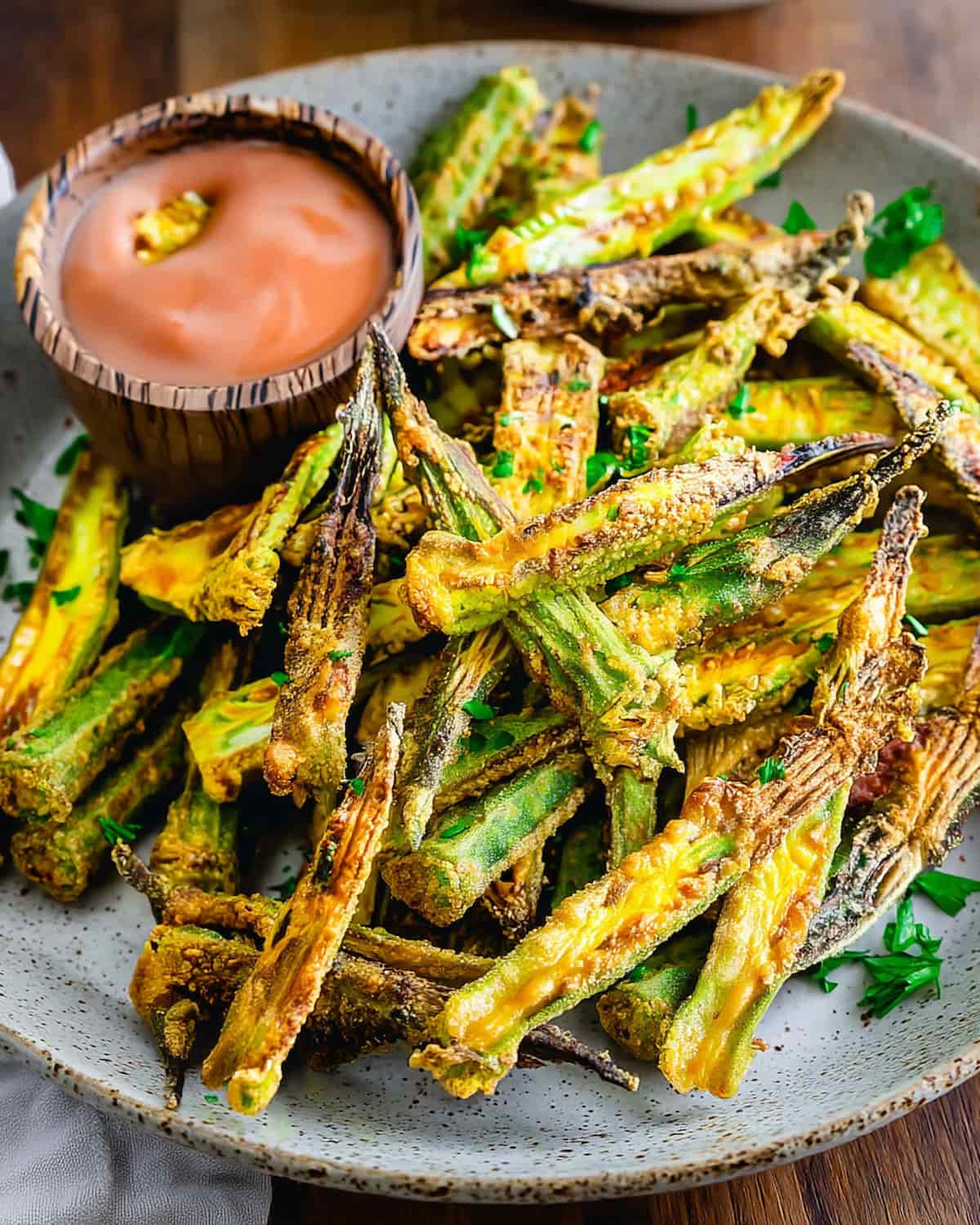 Air Fryer Okra with charred edges, garnished with fresh parsley, served on a gray plate with dipping sauce.