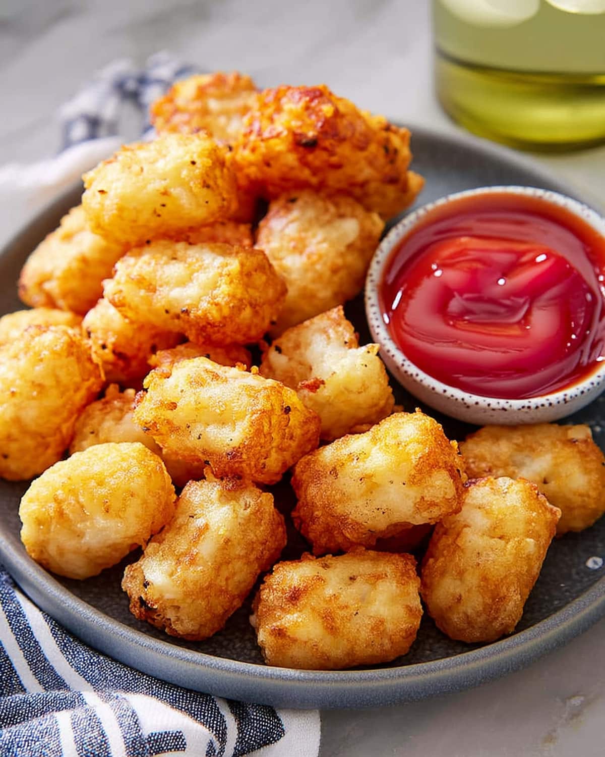 Air Fryer Tater Tots piled on a gray plate with ketchup for dipping.