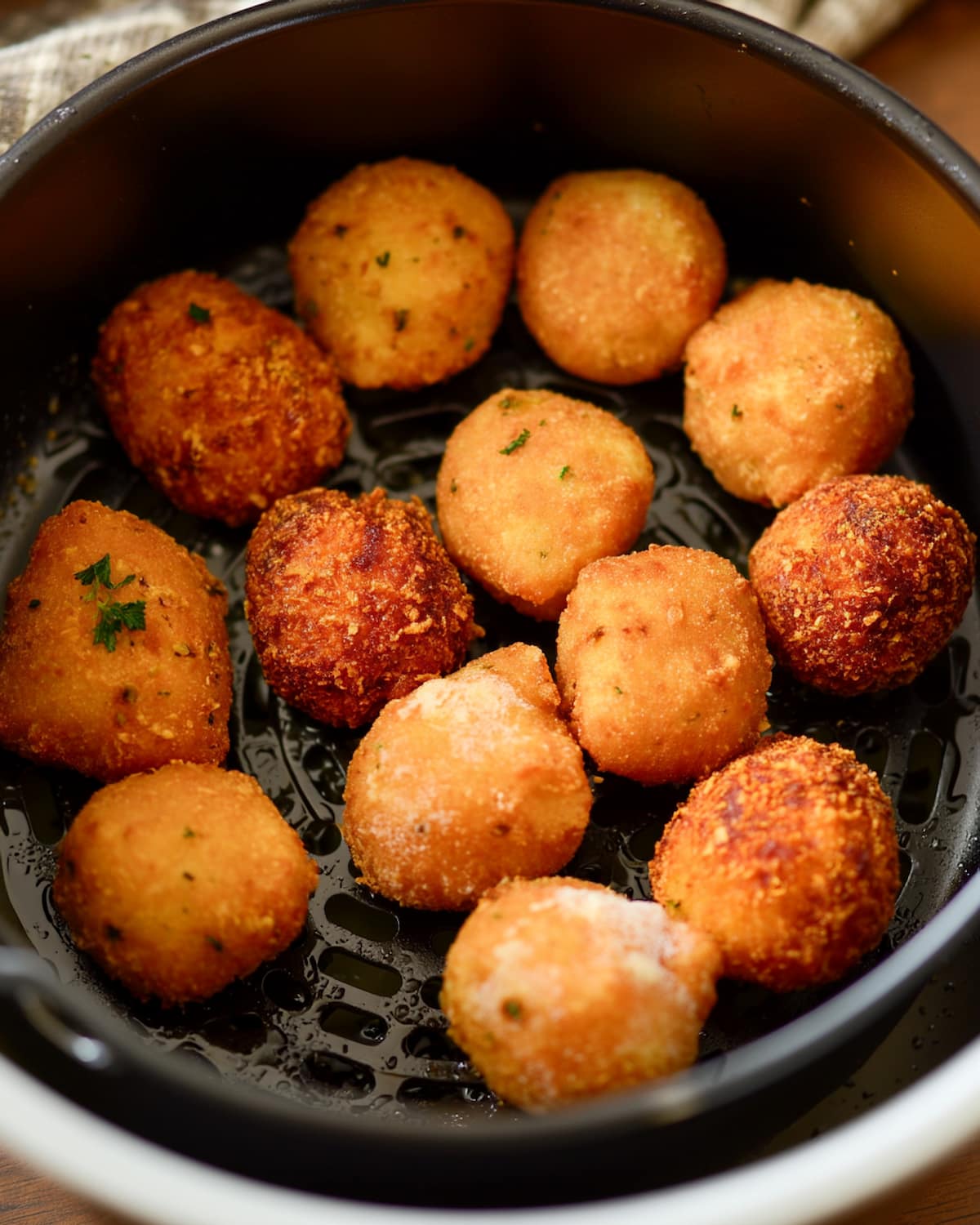 Golden frozen hush puppies resting in an air fryer basket, crispy and evenly browned