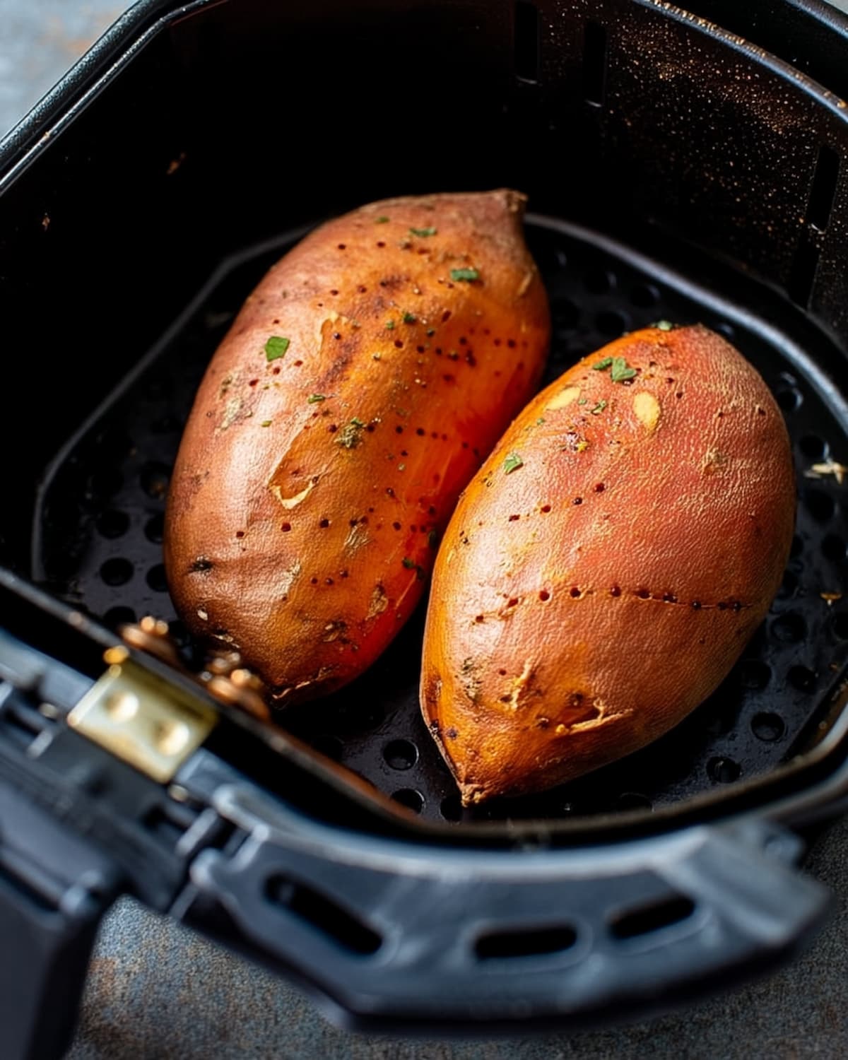 Two whole sweet potatoes resting in an air fryer basket with a soft and roasted skin