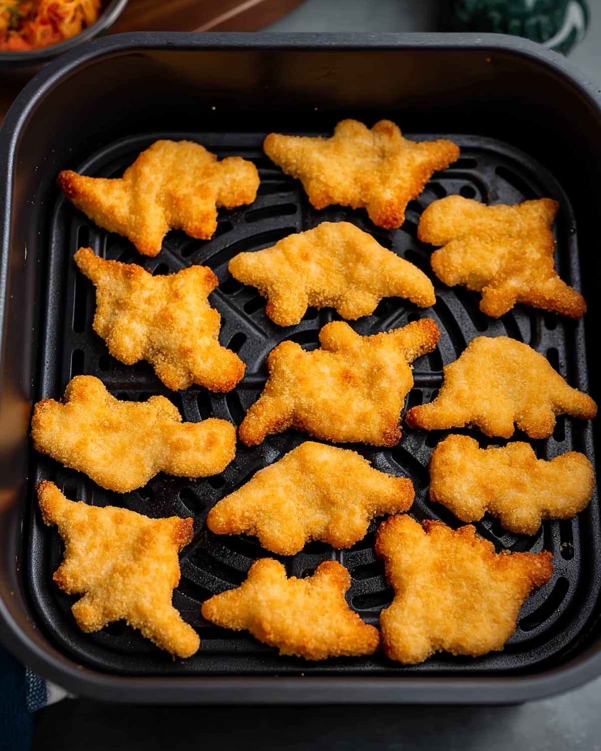 Crispy dino nuggets cooked in the air fryer for a quick family snack Golden dino nuggets arranged in an air fryer basket with a crisp breaded coating