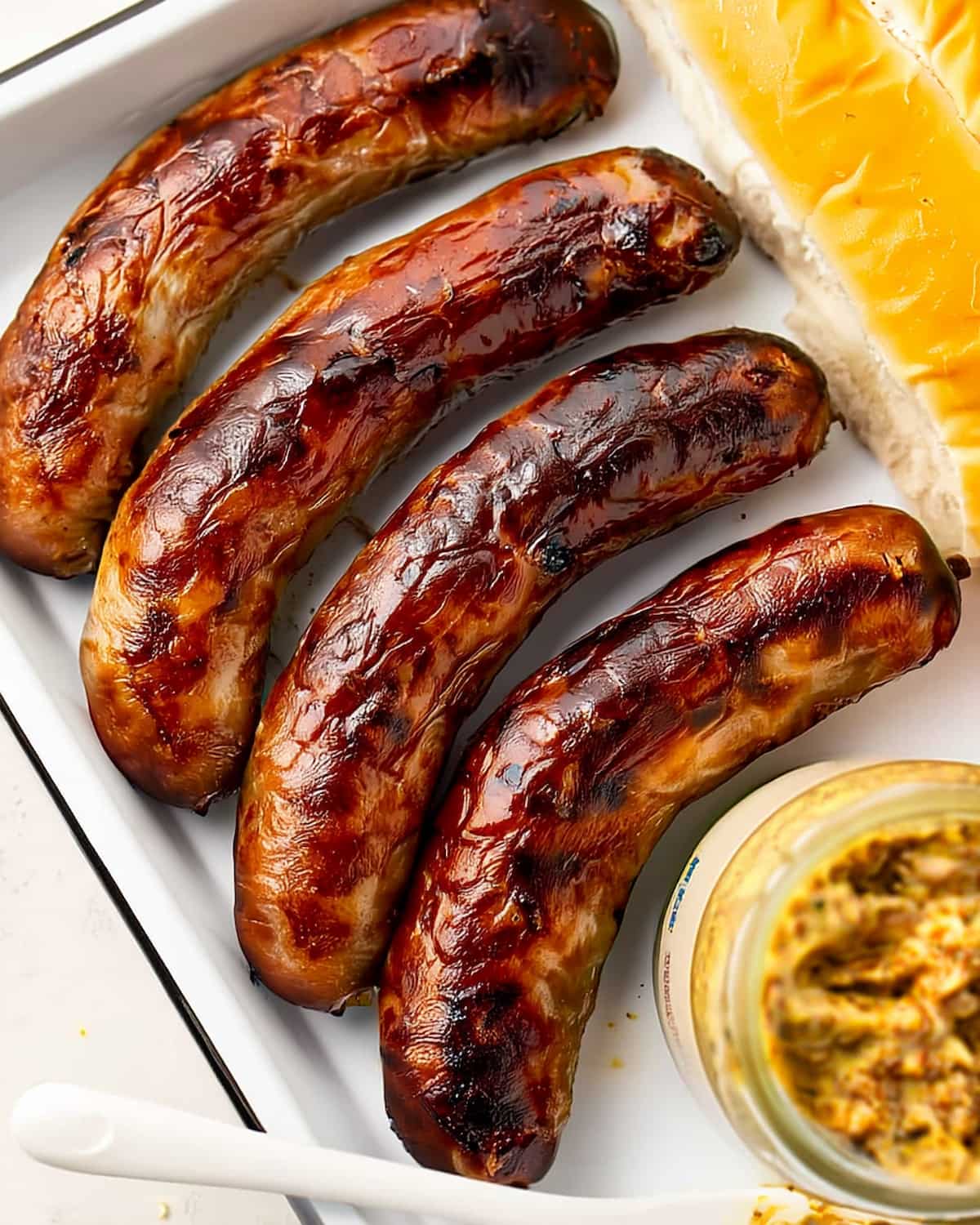 Sausage in Air Fryer with caramelized char marks, served on a white platter with mustard.