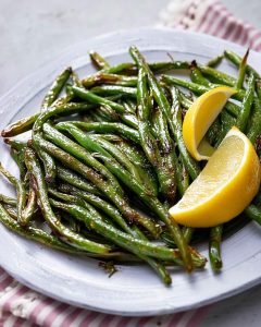 Air fryer green beans with charred edges and glossy finish, garnished with two lemon wedges.