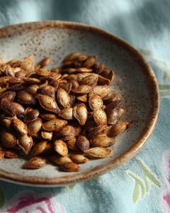 Air fryer butternut squash seeds with golden-brown seasoning on a speckled ceramic plate over a floral cloth.