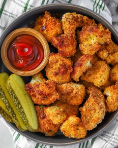 Air fryer gluten-free chicken nuggets with crispy golden coating, ketchup in wooden bowl, and pickle slices.