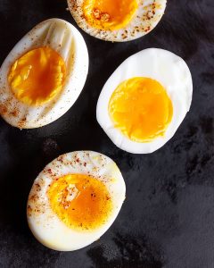 Air fryer jammy eggs on dark surface, showing golden runny yolks and firm whites, some seasoned.