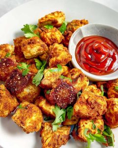 Air fryer tofu nuggets with crispy golden coating, fresh cilantro, and ketchup dipping sauce.