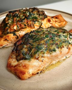 Crab stuffed salmon from air fryer on white plate, topped with herbs and melted cheese, glistening with butter sauce.