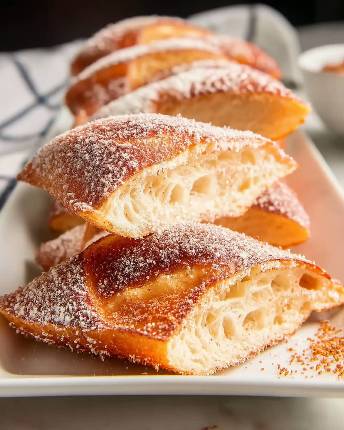 Air fryer churro pretzel bites dusted with powdered sugar on white plate, showing fluffy interior.